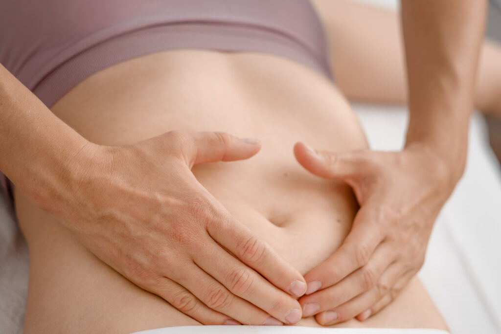 Hand der Therapeutin zu einem Herz geformt auf dem Bauch einer Patientin.